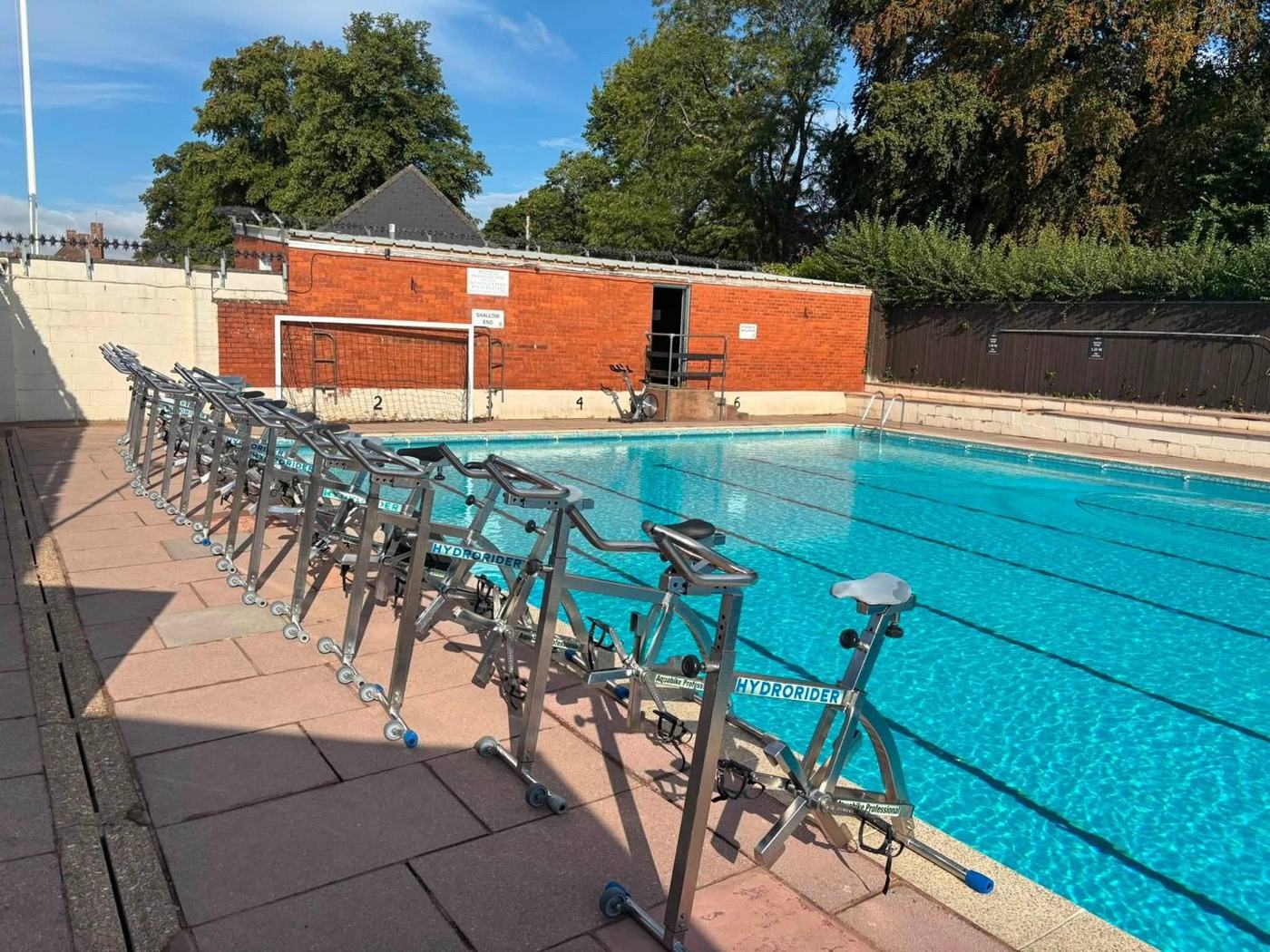 Aqua bikes lined up beside a sunlit outdoor pool before a class