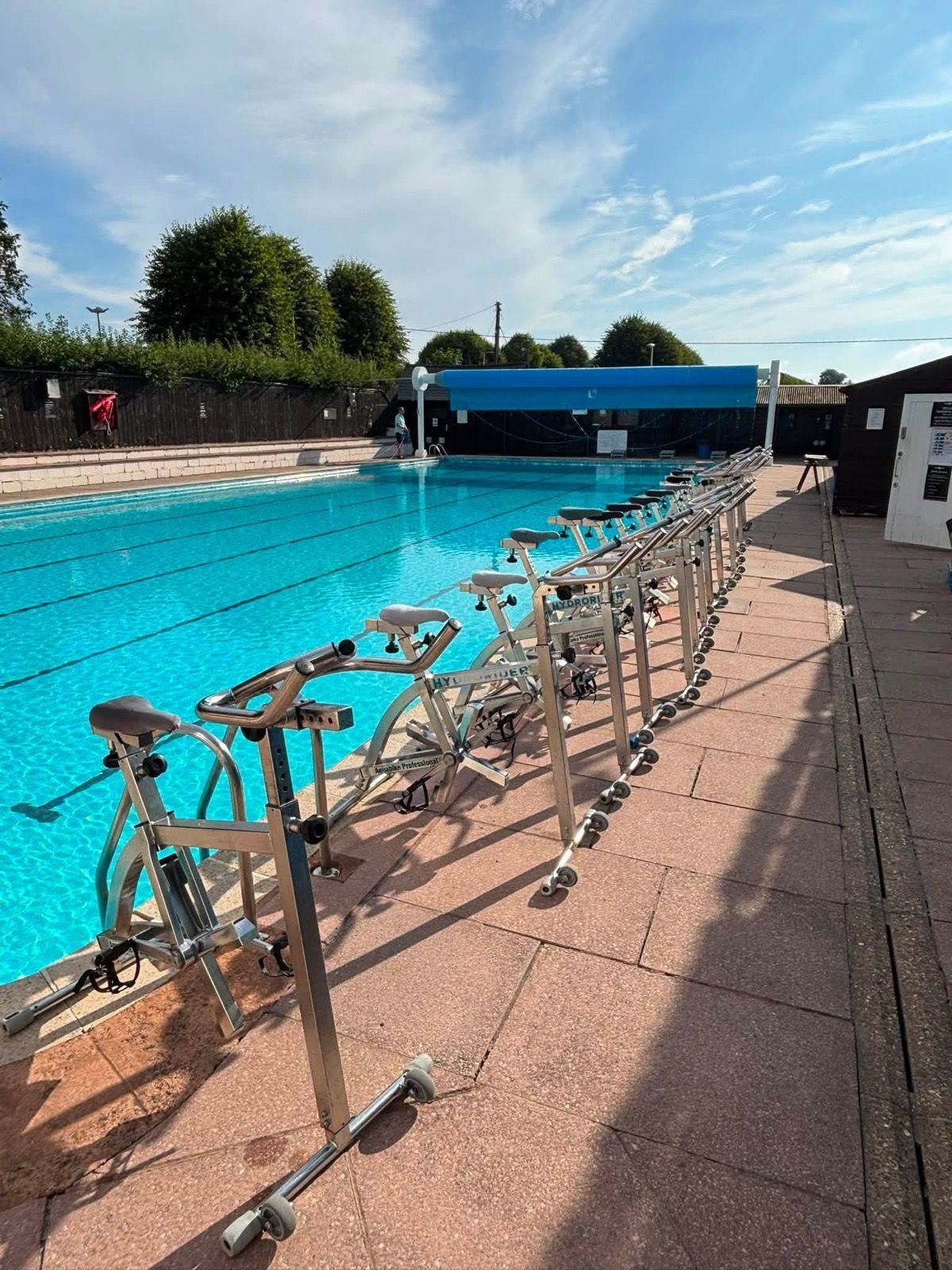 Aqua bikes lined up along the edge of an outdoor pool on a sunny morning