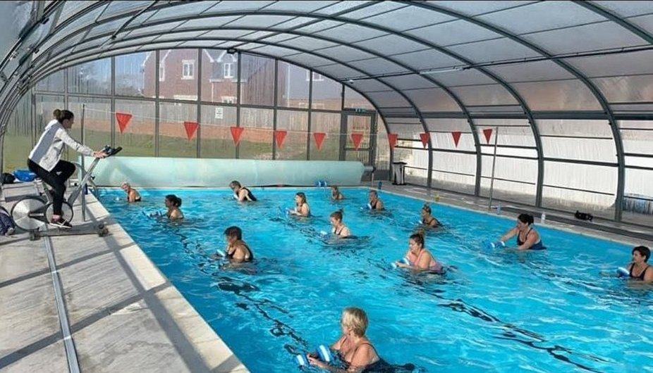 An instructor coaching a full Aquaspin class from the poolside while riders exercise in the water